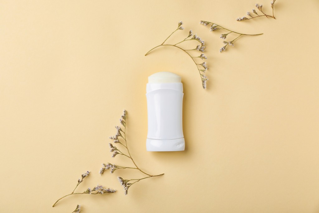 White deodorant and herbs on color background